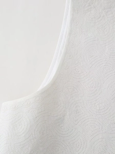 Détail du gilet blanc montrant la broderie géométrique et la texture matelassée fine
