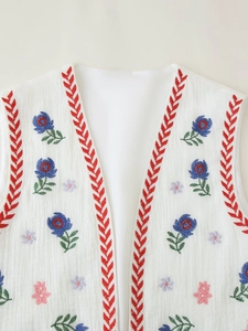 Detail of V-neck white vest showing blue floral embroidery and woven textured fabric