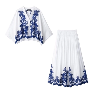 Broderies florales bleues sur chemisier blanc col V et jupe plissée assortie