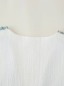 Detail of white round neck top featuring colorful Bohemian embroidery and crinkle texture