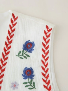 Detail of white embroidered vest featuring red geometric patterns and floral textures