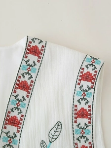 Close-up of white ethnic sleeveless top featuring colorful folk embroidery and linen texture