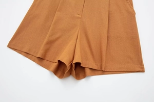 Detail of high-waist wide-leg linen shorts in ochre with pleated waist and fine stitching