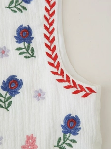 Detail of white sleeveless vest featuring colorful floral embroidery and textured fabric