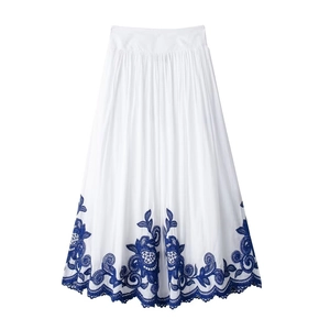 Détail d'une jupe longue blanche avec broderie florale bleue et tissu plissé élégant
