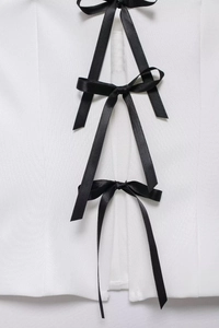 Detail of white off-shoulder top featuring black satin bow ties and woven fabric texture