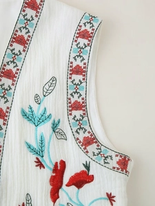 Macro detail of white textured vest featuring intricate bohemian floral embroidery on fabric