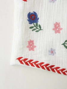 Detail of colorful floral embroidery on white pleated fabric with ethnic red trim