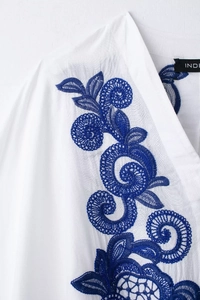 Détail d'une broderie florale bleue sur une chemise d'été blanche à texture fine