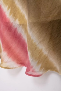 Dettaglio del tessuto tie-dye trasparente con motivi bordeaux e ocra dell'abito midi