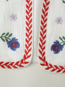 Detail of white crinkle vest featuring colorful floral embroidery and textured fabric