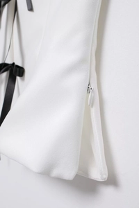 Detail of white off-shoulder top with hidden side zipper and black ribbon bow accent