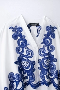 Détail de la broderie florale bleue sur la chemise blanche à manches longues et col V