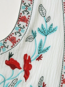 Macro shot of ethnic embroidery with red flowers and blue leaves on white linen vest