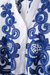 Détail de la broderie bleue complexe sur une chemise d'été blanche aux motifs élégants
