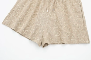 Detailed close-up of white floral embroidery on beige linen shorts with metal tipped drawstring