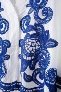 Détail de la broderie florale bleue sur chemise blanche en coton avec couture soignée