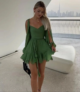 Detail of the emerald green mini dress with pleated fabric and cape-style long sleeves