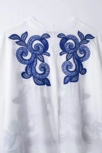 Détail de la broderie florale bleue sur le tissu blanc d'une blouse en coton et lin