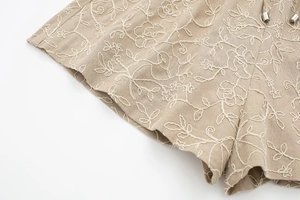 Detail shot of khaki summer shorts showing white floral embroidery and cotton linen texture