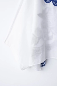 Détail de chemisier blanc avec broderie florale bleu foncé au col et à l'ourlet