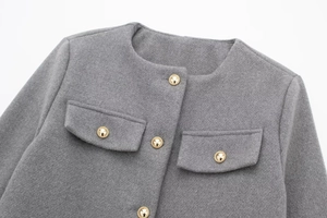 Detailaufnahme der grauen Tweedjacke mit goldgeprägten Knöpfen und feiner Stoffstruktur