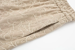 Detail of elastic drawstring waist and white floral embroidery on beige casual shorts