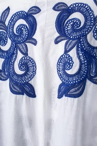Gros plan détaillé d'une broderie florale bleue sur une chemise en coton lin blanc
