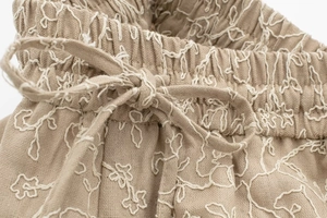 Close-up of elastic drawstring waist with white floral embroidery on khaki fabric