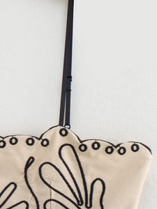 Dettaglio di un abito in lino beige con ricamo floreale nero e spalline regolabili