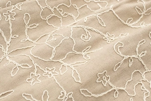 Detailed close-up of floral embroidery on beige linen cotton fabric texture