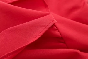 Macro detail of red woven fabric showing precise stitching and hem texture for crop top