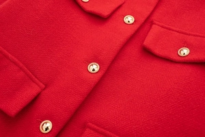 Nahaufnahme des roten Tweed-Stoffs mit eleganten geprägten Goldknöpfen an der Jacke