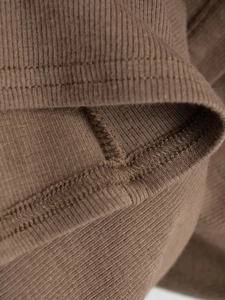 Gros plan détaillé du tricot côtelé marron montrant une finition à double aiguille de qualité