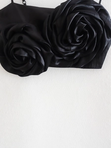 Detailed macro view of black satin crop top featuring dual 3D dimensional rose flower accents