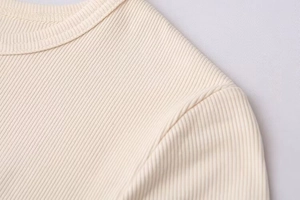Close-up of cream ribbed knit fabric showing fine texture and round neckline detail