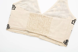 Detail view of cream halter top featuring smocked elastic back and ethnic black embroidery
