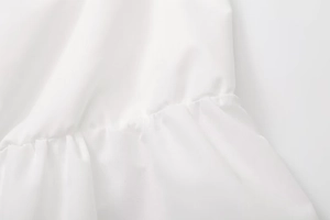 Macro detail of white pleated ruffle hem and stitching on a slim-fit summer crop top