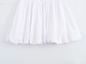 Détail de la robe blanche montrant l'ourlet bulle plissé et le tissu en coton structuré