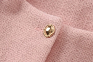 Nahaufnahme einer rosa Tweed-Jacke mit einem verzierten goldenen Knopf im Vintage-Stil