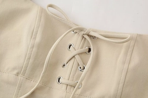Detail of beige midi dress featuring lace-up design with silver metal eyelets and twill fabric