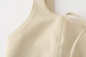 Detailed macro view of cream cotton fabric texture and strap stitching on midi dress