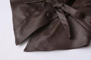 Detail of dark brown faux leather coat featuring a tied waist belt and matching button