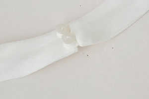 Detailed close-up of a white satin dress featuring two translucent round buttons at the neckline