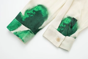 Détail de manchette de chemise avec imprimé artistique vert et bouton sur tissu crème