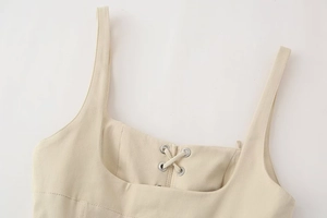 Detail of beige midi dress featuring a square neckline with criss-cross lacing and metal eyelets