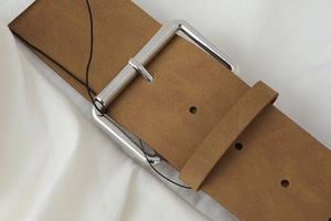 Detail of a brown leather belt with a large silver metal buckle and textured strap