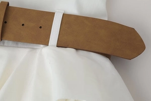 Close-up of brown faux leather belt with punched holes on a white summer dress