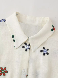 Détail de la broderie florale sur le col et boutons blancs sur chemise en coton beige