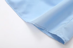 Detailed close-up of light blue fabric texture and professional hem stitching craftsmanship